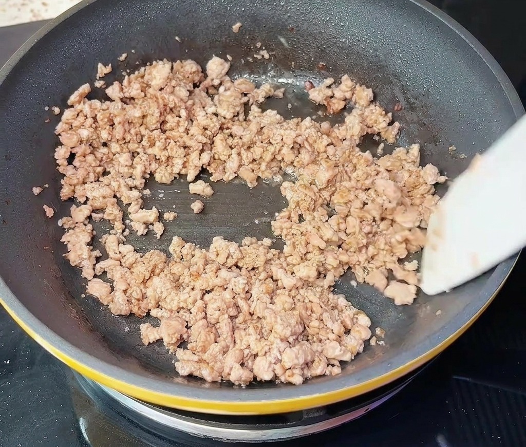 Minced beef being stirred in a skillet with a white spatula, appearing fully browned and crumbled.