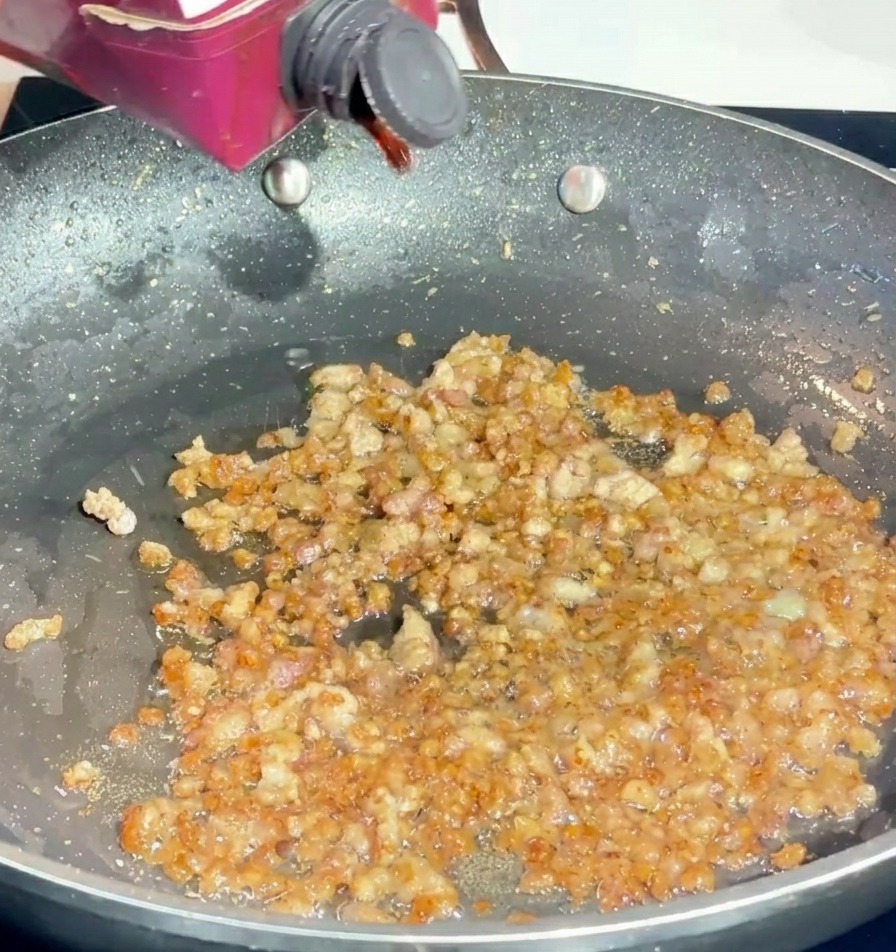 Pouring red wine from a small carton into a pan of browned minced pork.