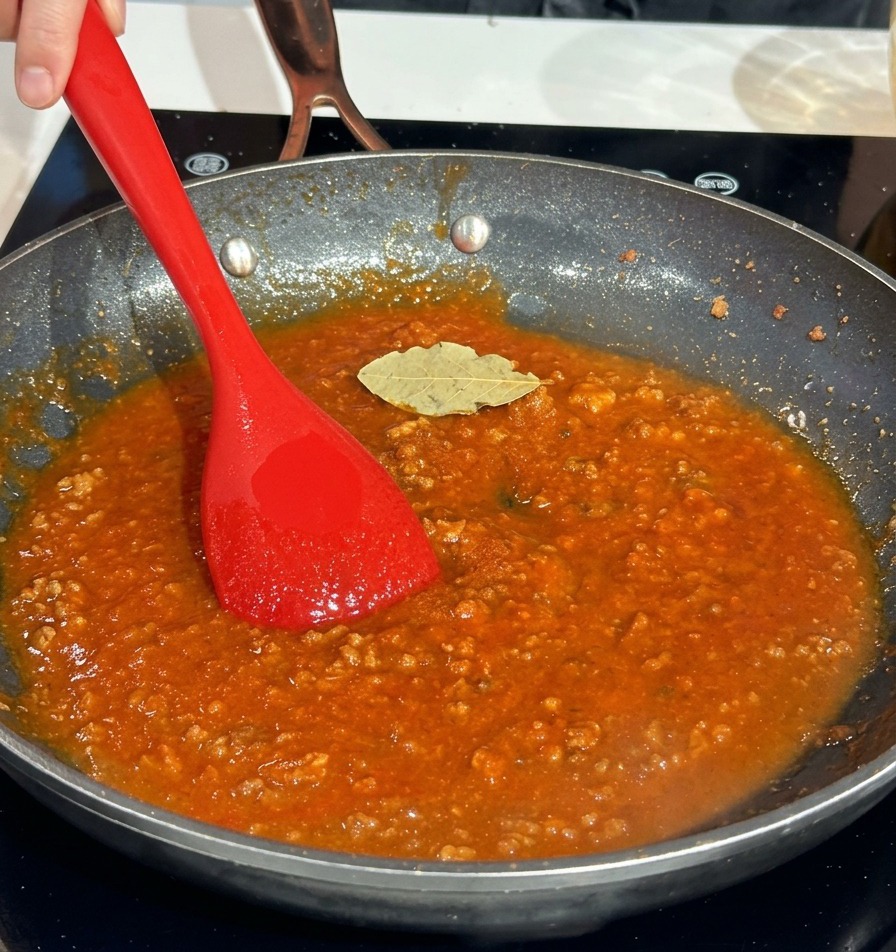 A dried bay leaf resting on top of a rich red meat sauce in a frying pan.