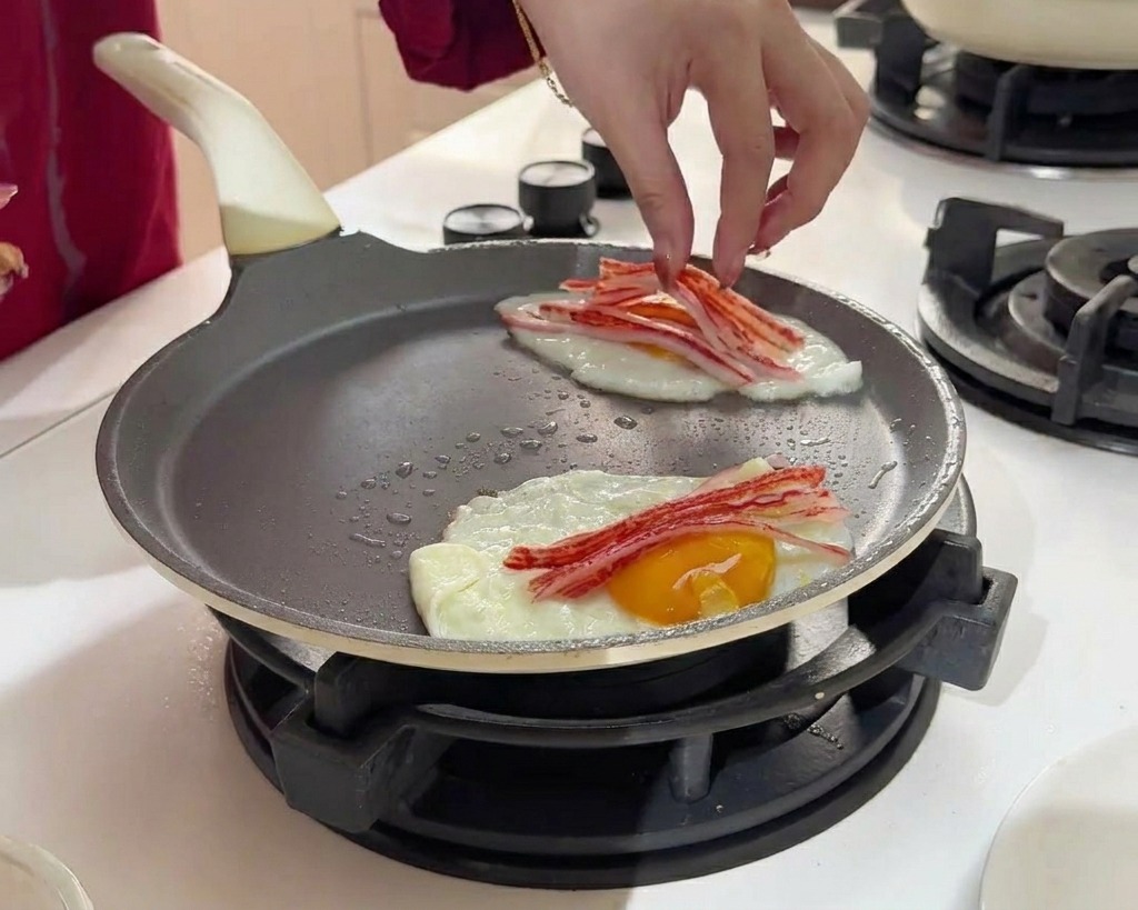 Placing thin strips of red and white crab sticks onto the surface of two cooking fried eggs.