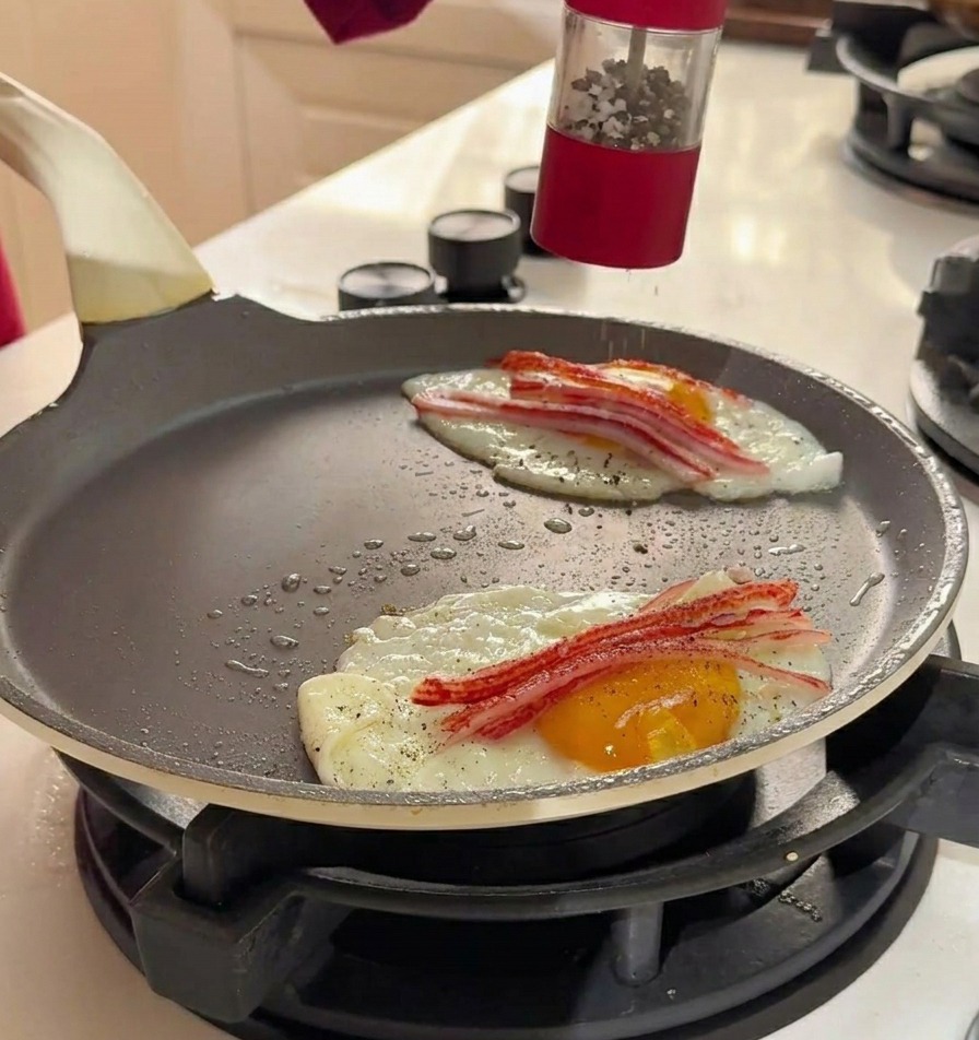 Grinding sea salt and black pepper from a red manual grinder over the eggs and crab sticks in the pan.