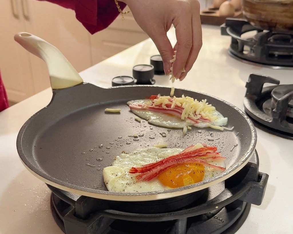 A hand sprinkling shredded white cheese over the cooking eggs and crab sticks.