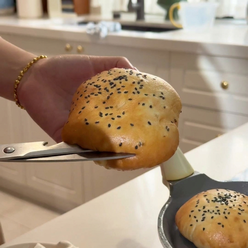 A hand carefully slicing open a warm sesame seed bun using silver kitchen scissors.