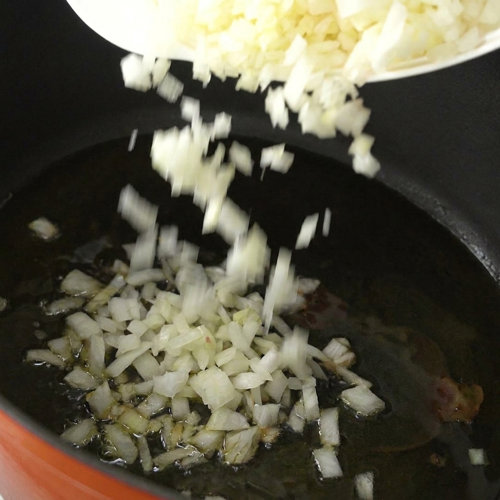 Finely diced white onions falling from a white plate into a pot of hot oil.