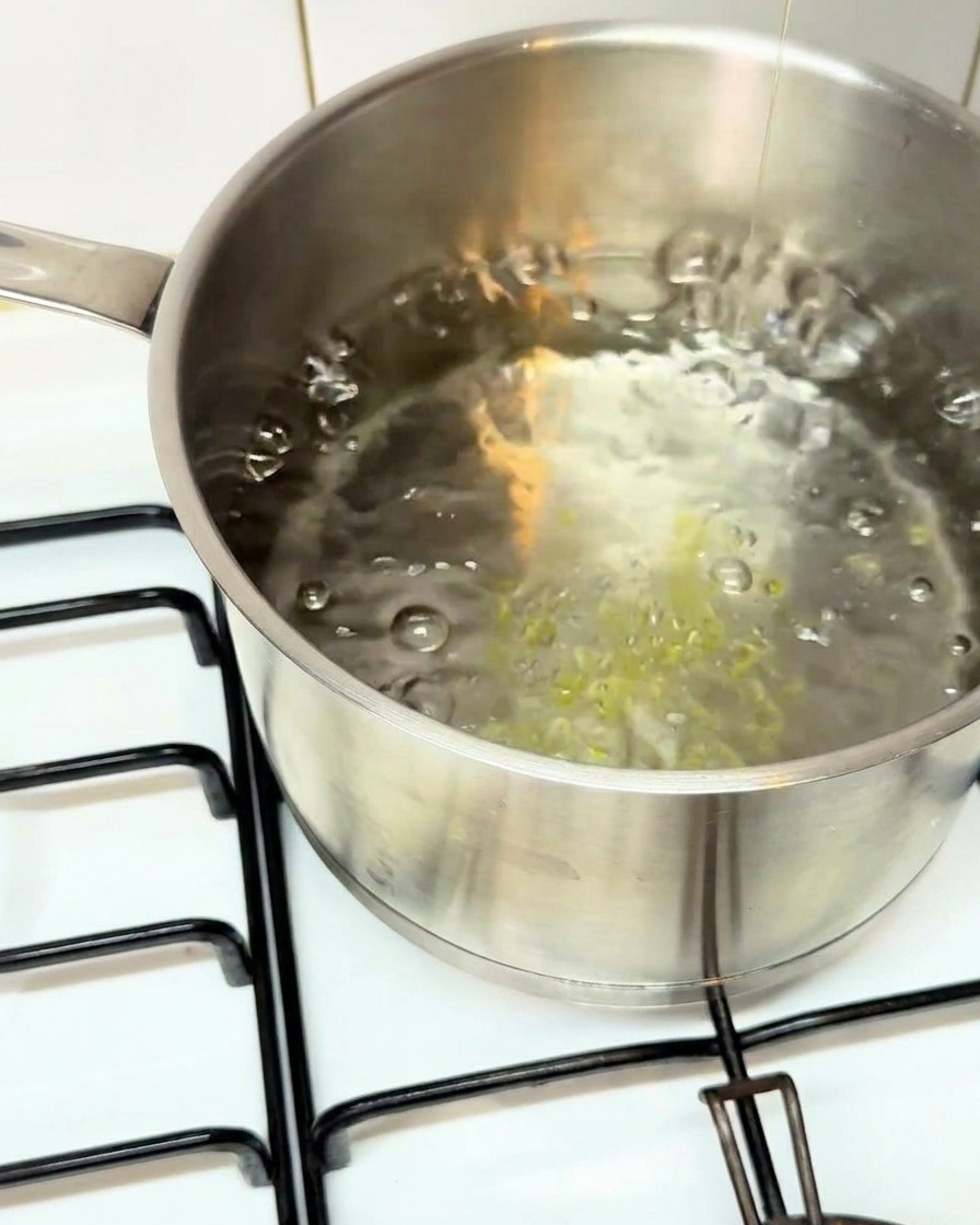 Thick paccheri pasta tubes being dropped into a stainless steel pot of rapidly boiling water.