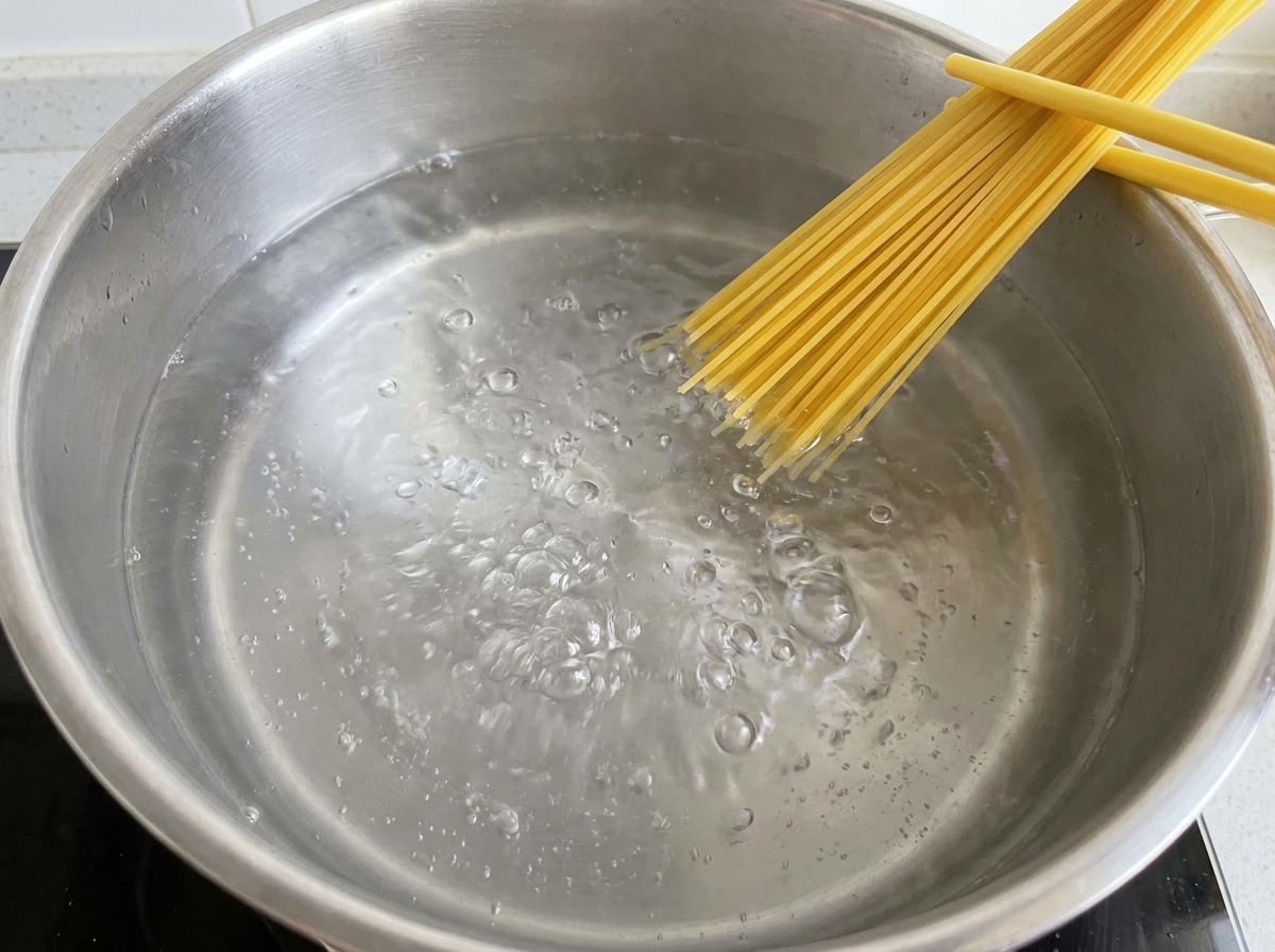 Dry spaghetti noodles being submerged into a pot of actively boiling water.