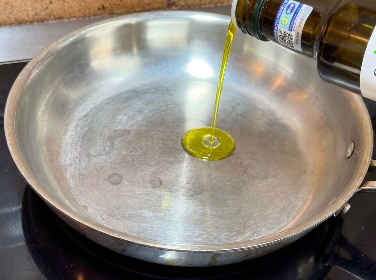 Extra virgin olive oil being poured from a bottle into a flat-bottomed metal frying pan.