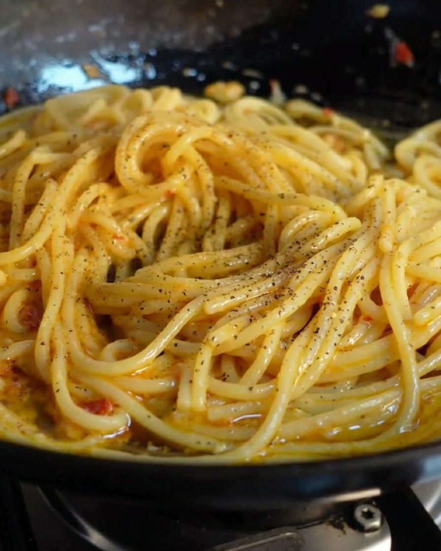 Freshly ground black pepper sprinkled over a pan of glossy spaghetti.