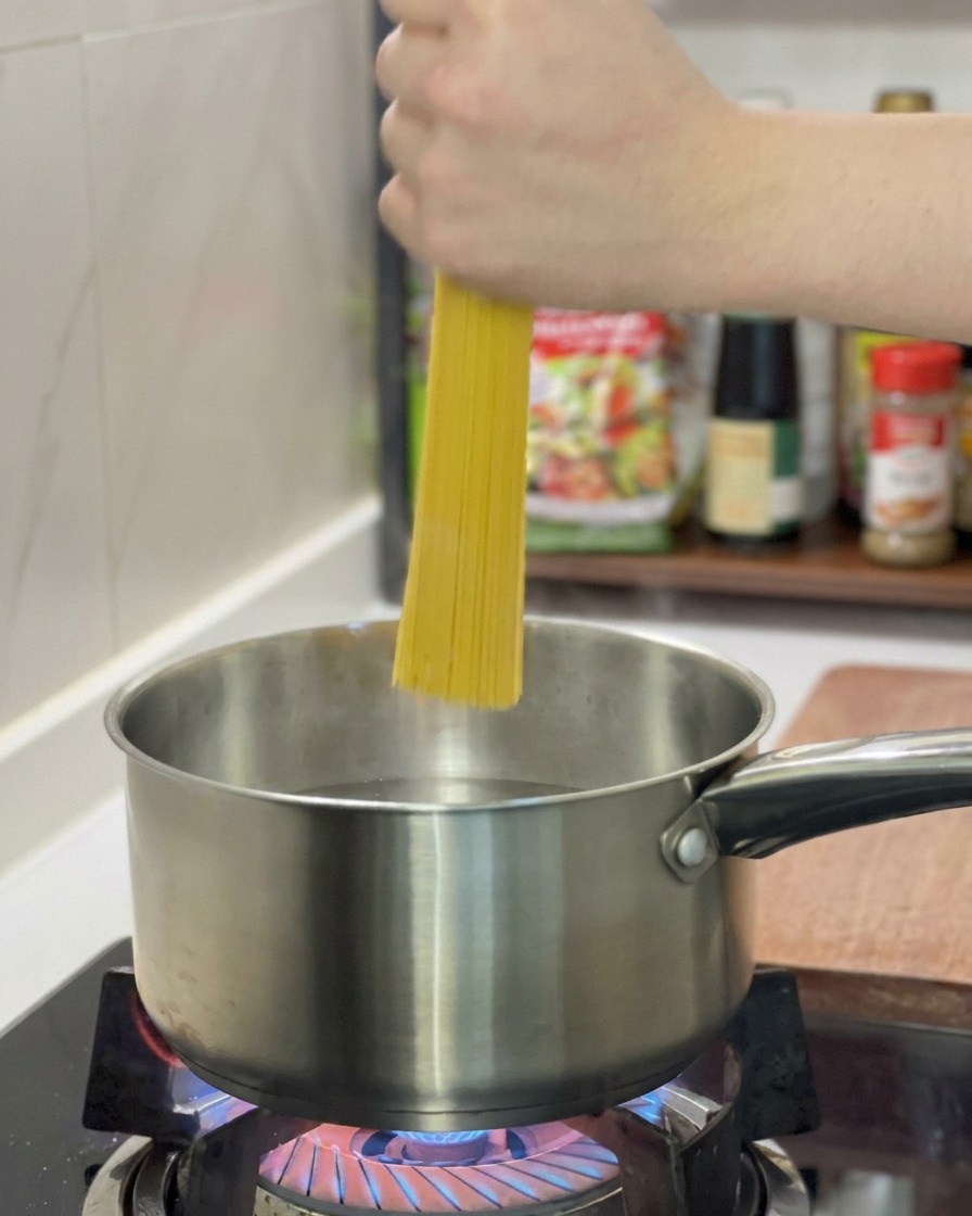 A hand holding a bunch of dry spaghetti upright as it is being placed into a stainless steel pot of boiling water.