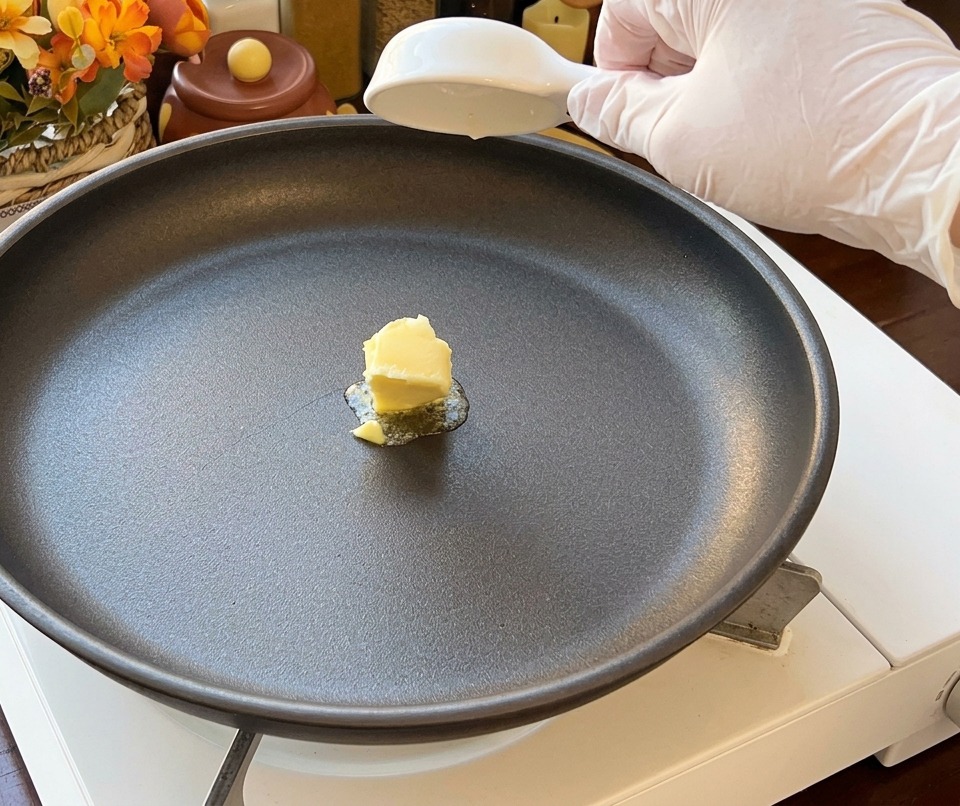 A small pat of yellow butter melting in the center of a black non-stick skillet on a portable stove.