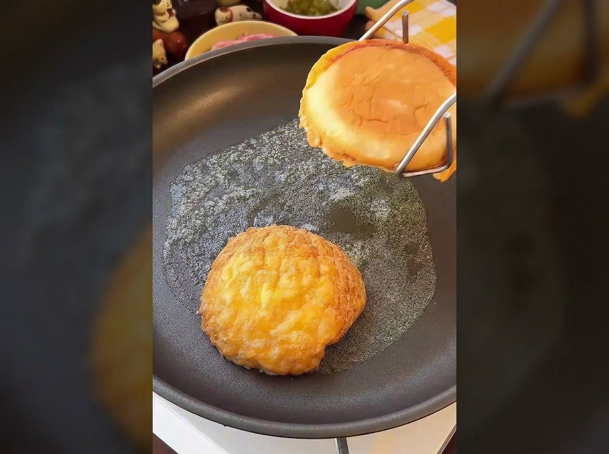 Two halves of a burger bun being toasted face-down in a buttery frying pan until golden and crisp.