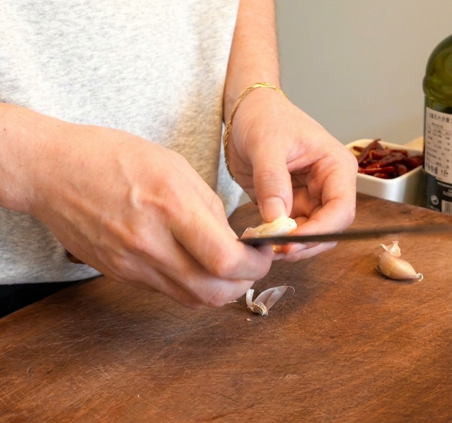 A person holding a garlic clove and slicing it in half with a knife to remove the inner germ.