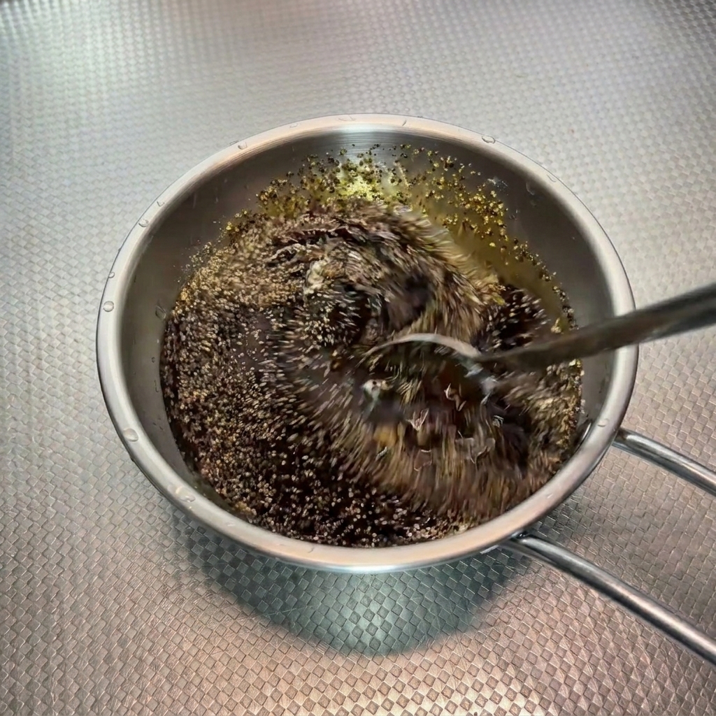 A dark black pepper sauce mixture being stirred rapidly with a spoon in a metal bowl.