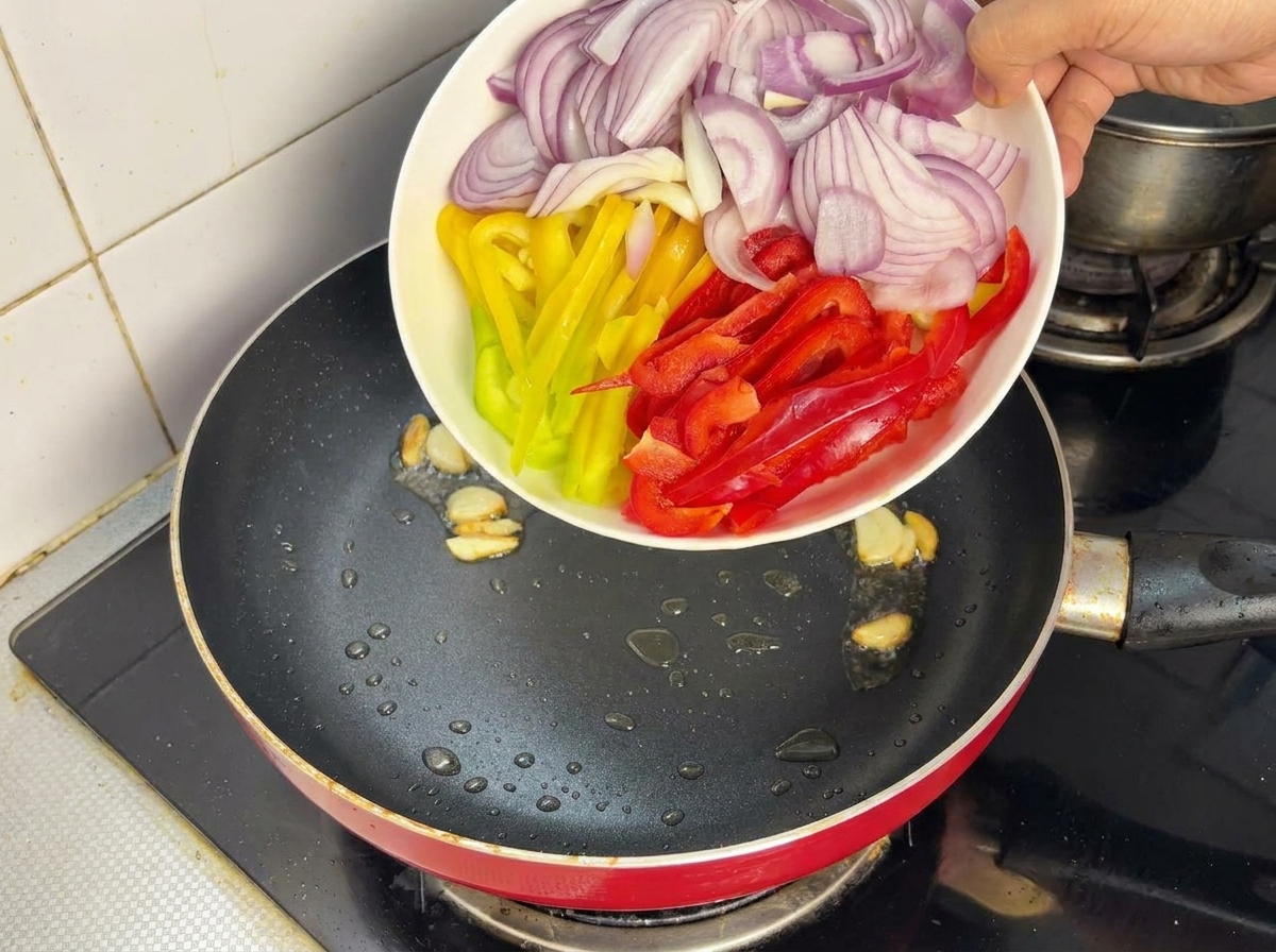 Sliced red onions and colorful bell peppers being added from a plate into a hot pan with oil.