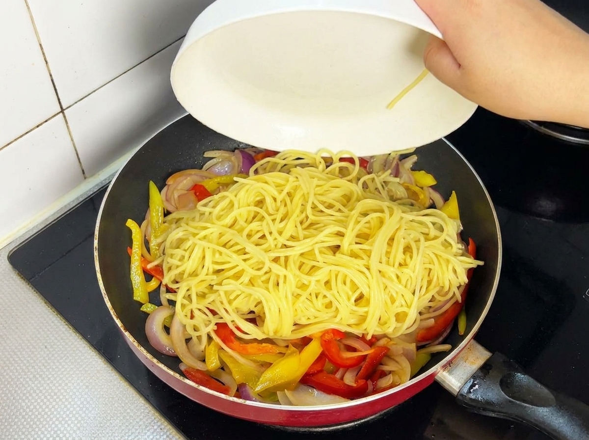 Cooked beef slices being added back into a frying pan containing spaghetti and vegetables.