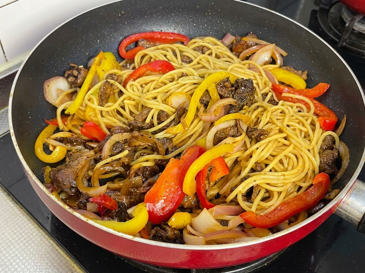 Black pepper spaghetti, beef slices, and colorful bell peppers thoroughly mixed and coated in sauce in a frying pan.