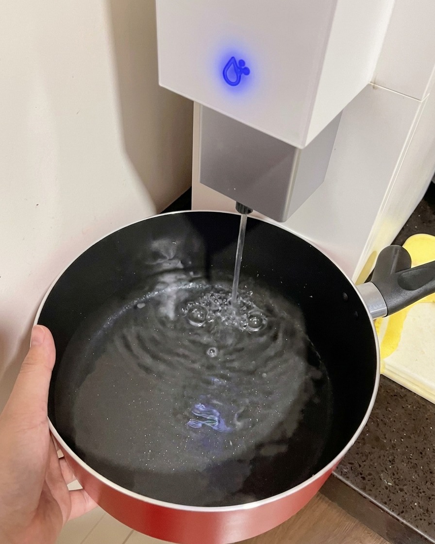 A hand holding a red pot as it fills with water from a water dispenser.