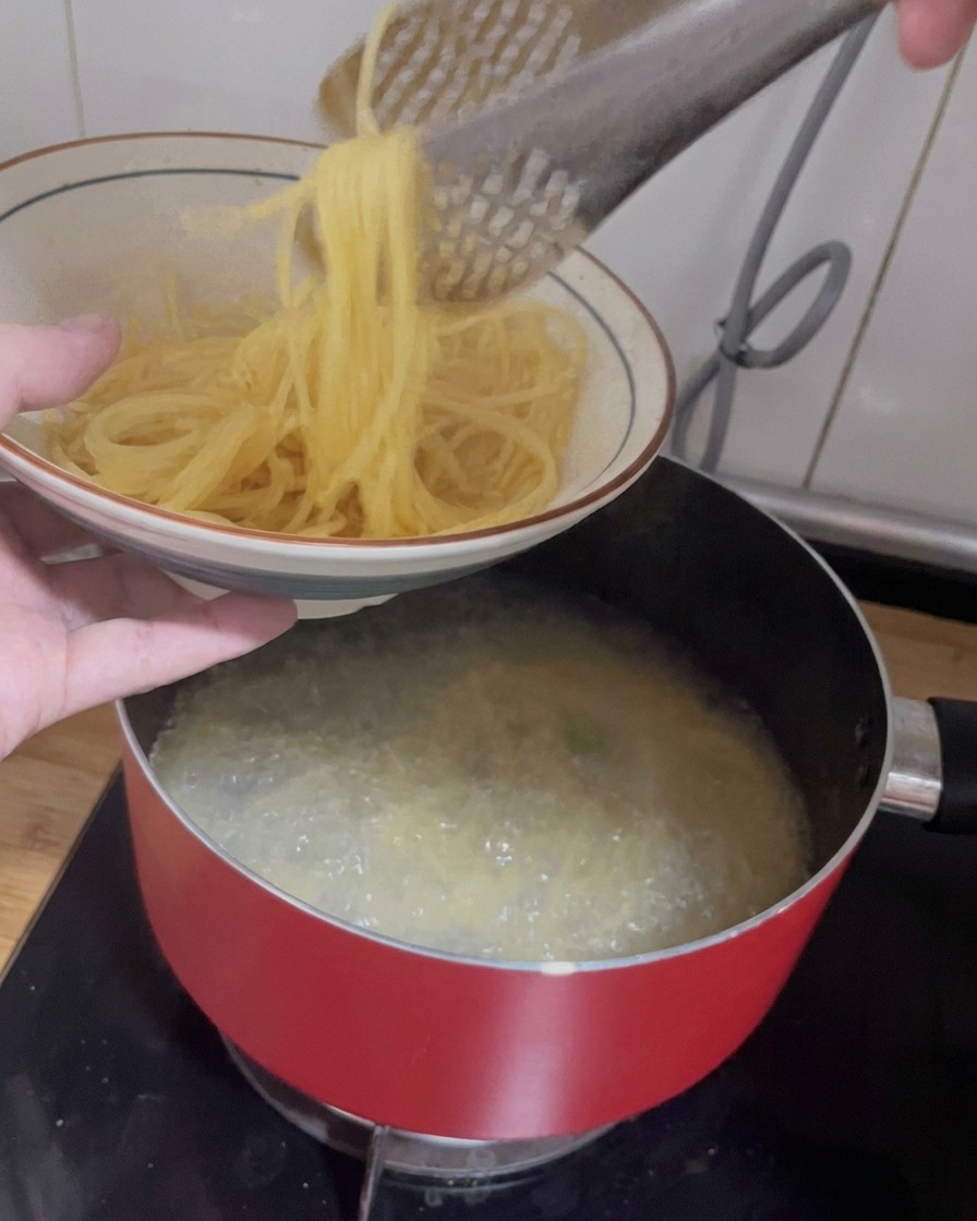Tongs lifting cooked spaghetti out of a pot of boiling water into a patterned ceramic bowl.