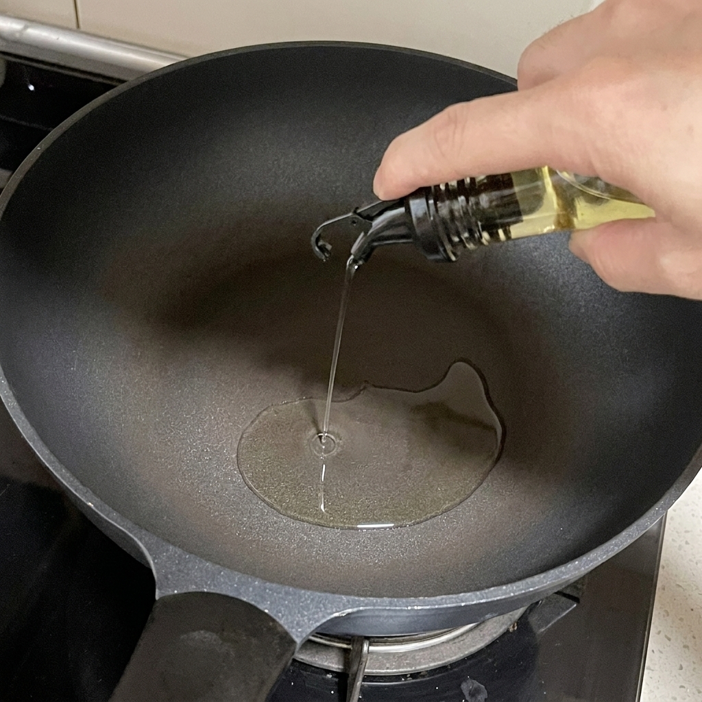 Cooking oil being poured from a glass dispenser into a dark skillet on a stovetop.