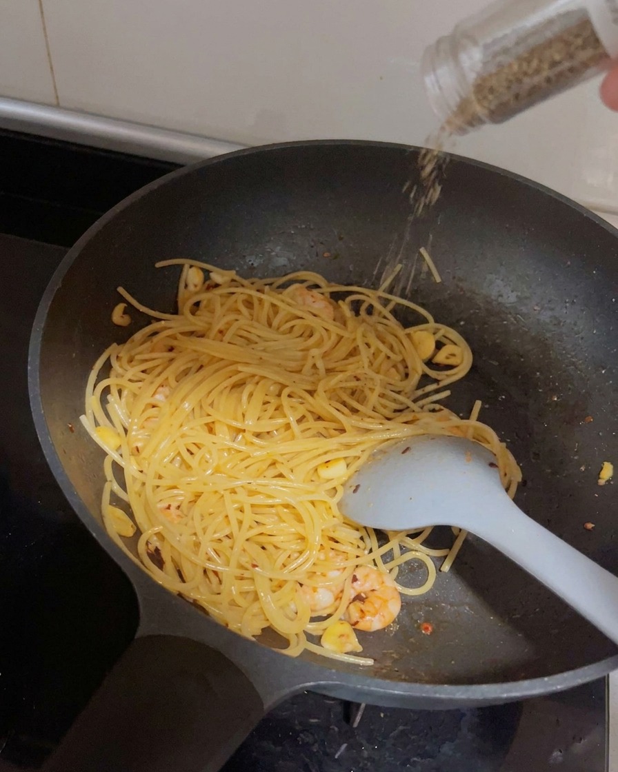 A grinder dispensing fresh black pepper over a pan of spaghetti and shrimp.