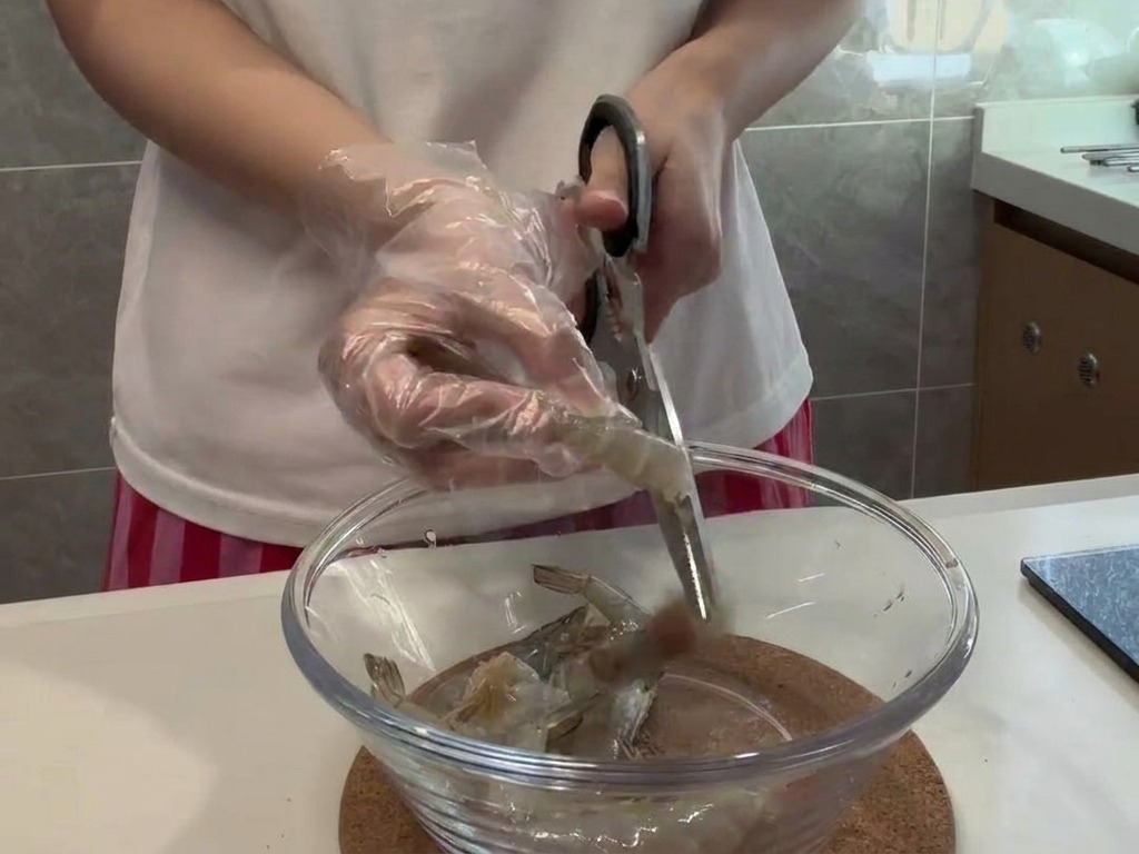 A person wearing gloves using scissors to carefully cut the back of a raw shrimp.
