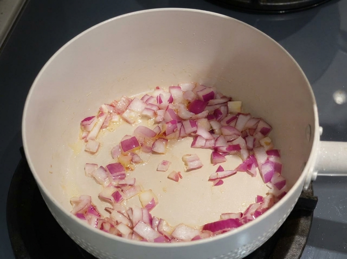 Chopped red onions being sautéed in oil in a light-colored pan.