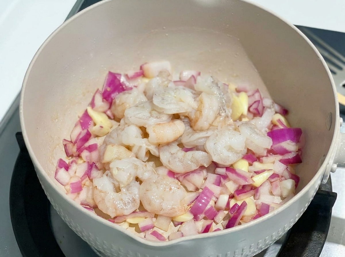 Raw, deveined shrimp added to a pan with sautéed red onions.