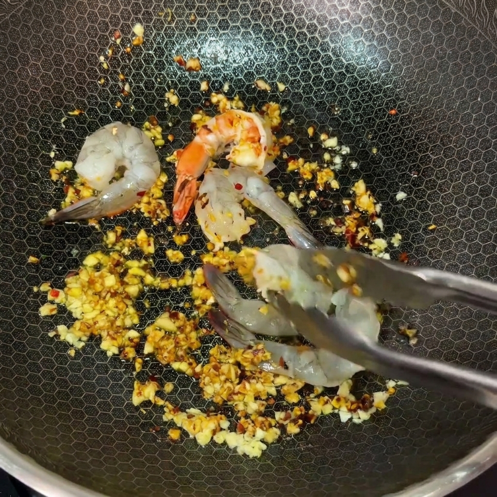 Using metal tongs to place raw shrimp into a hot wok filled with garlic and chili butter.