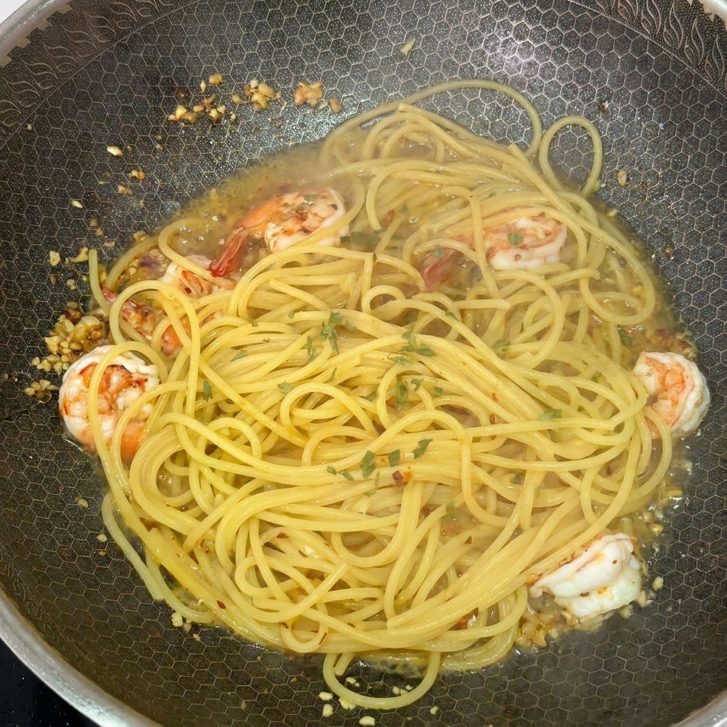 Spaghetti and shrimp in a hot wok being garnished with freshly chopped green parsley.