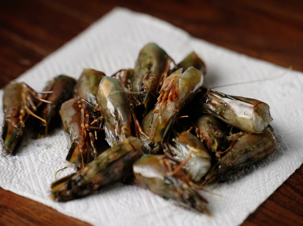 A pile of raw shrimp heads resting on a white paper towel to absorb excess moisture.