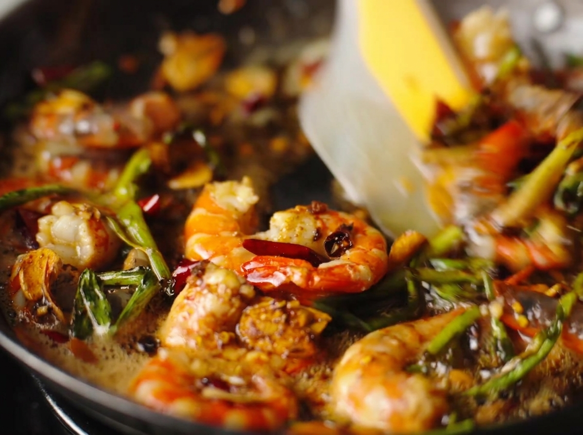 Peeled shrimp being sautéed with garlic, dried chilies, and scallions in a sizzling pan.
