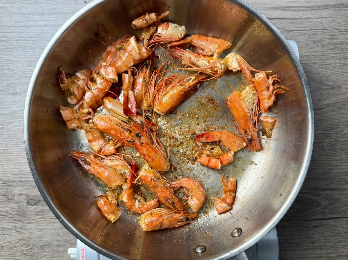 Shrimp shells frying in hot oil inside a stainless steel skillet.