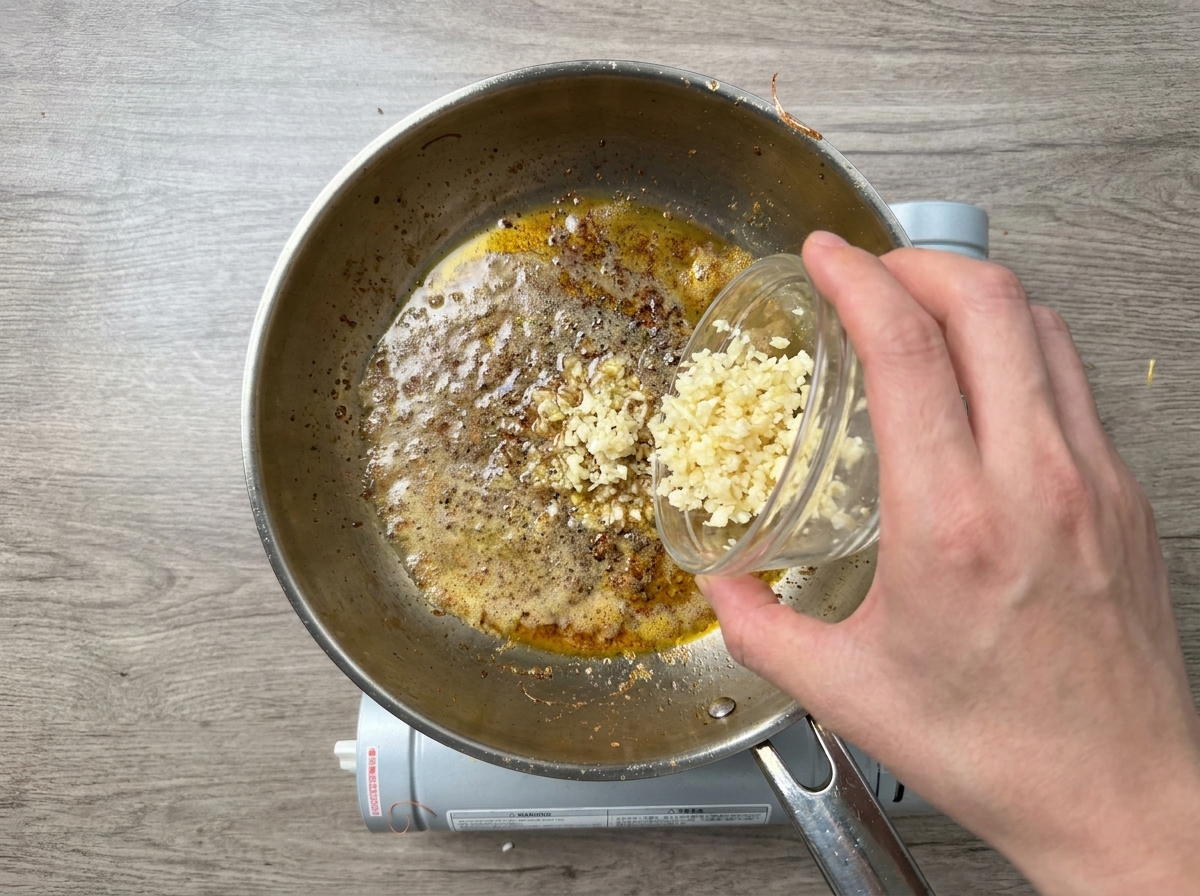Minced garlic being poured from a small glass bowl into a hot pan with melted butter and cooking oil.