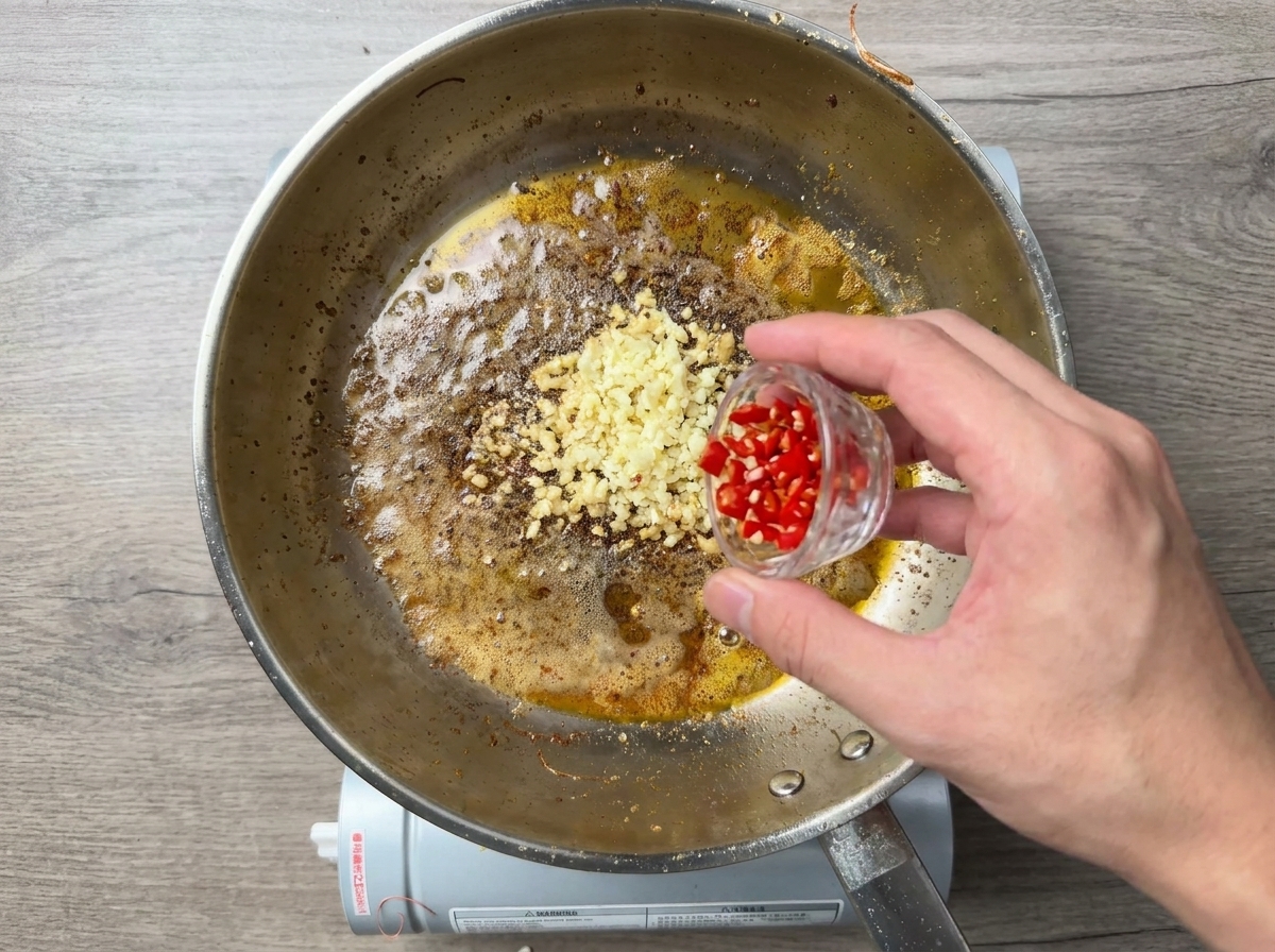 Chopped red chilies being added to a pan of sizzling minced garlic.