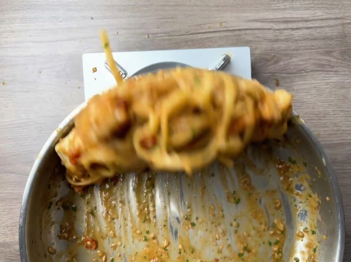 Linguine pasta and shrimp being tossed vigorously in a pan, creating motion blur.