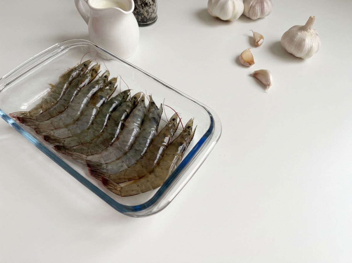 Raw, translucent grey shrimp lined up in a rectangular glass dish.