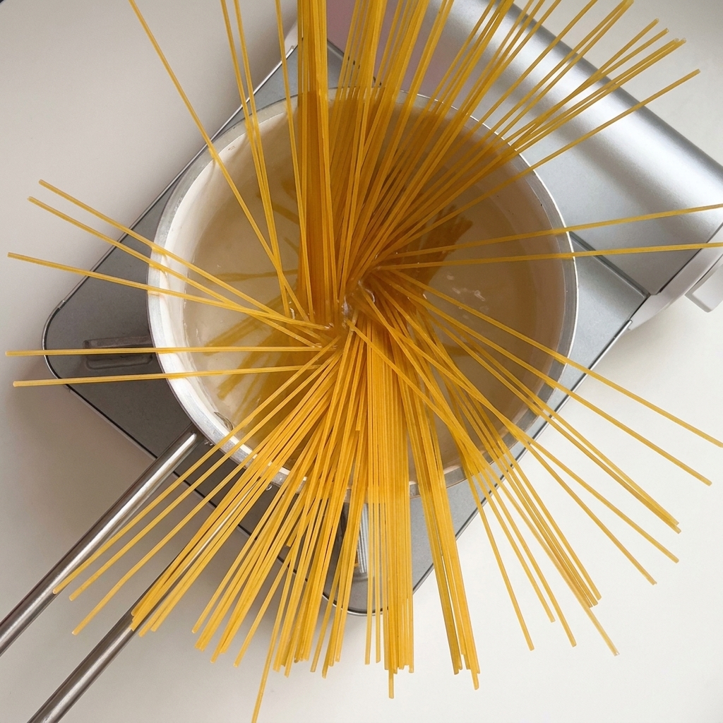 Dry spaghetti noodles fanned out in a pot of boiling water.