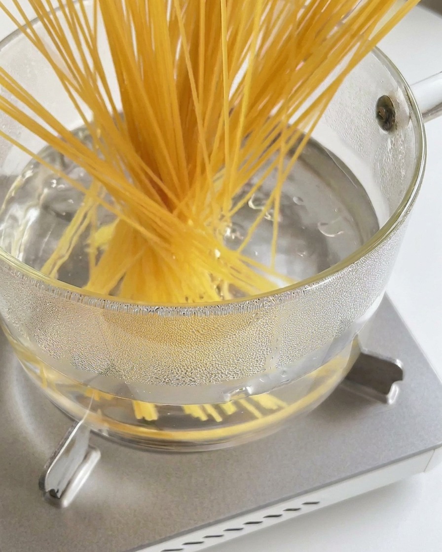 A bundle of long, dry spaghetti noodles being lowered into a glass pot of boiling water.