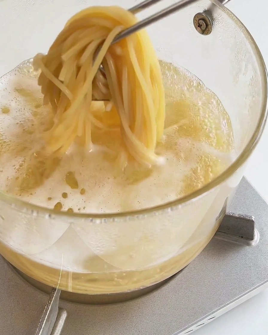 Kitchen tongs lifting a portion of cooked, soft spaghetti out of boiling water in a pot.