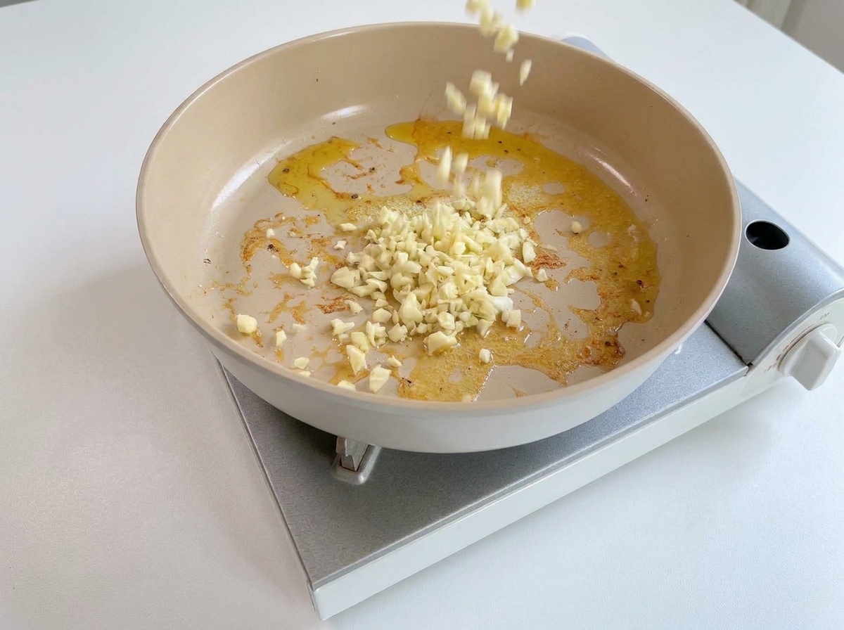 Chopped minced garlic falling into a warm pan with residual oil and butter.