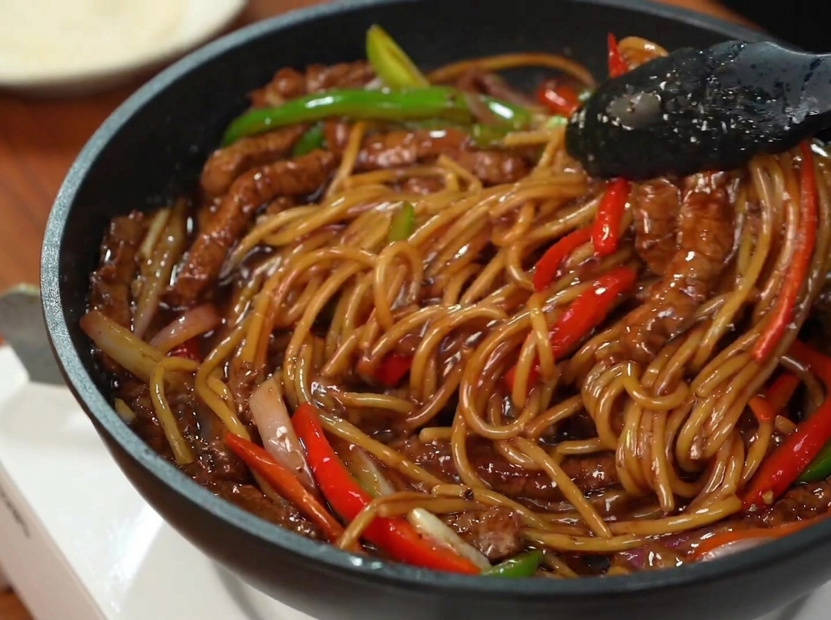 A serving of cooked pasta with beef and bell peppers arranged on a plate and topped with chopped parsley.
