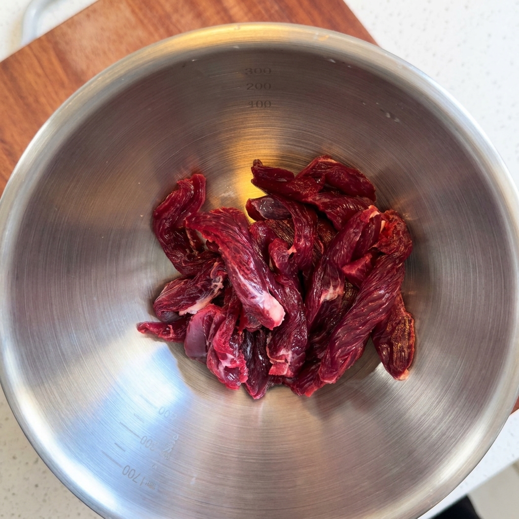 Raw beef tenderloin strips sitting in a stainless steel mixing bowl.
