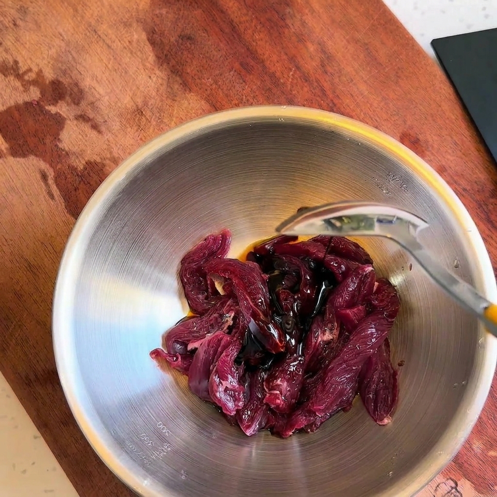 Adding dark liquid seasonings over raw beef strips in a bowl with a spoon.