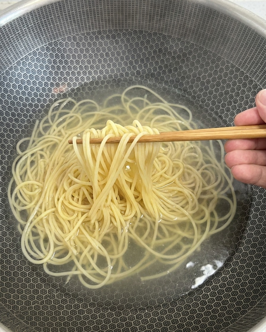 Cooked spaghetti noodles being lifted out of a pot of hot water with wooden chopsticks.