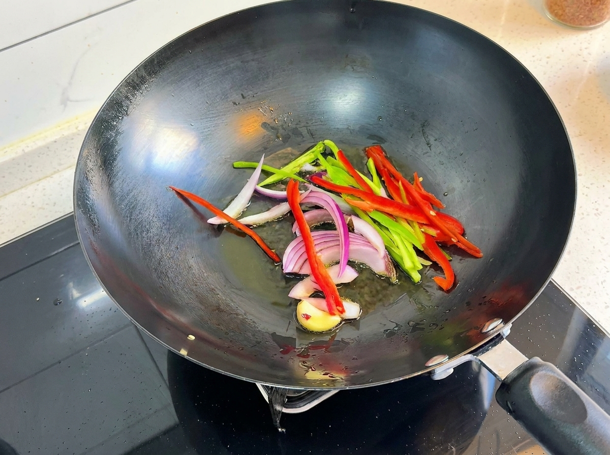 Sliced green and red bell peppers, red onion strips, and garlic pieces sizzling in a hot wok.