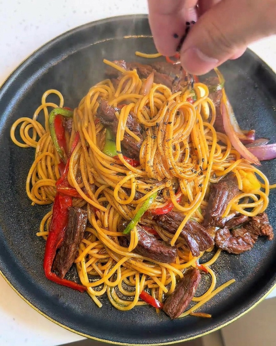 A hand carefully sprinkling black sesame seeds over a freshly plated, steaming dish of black pepper beef spaghetti.