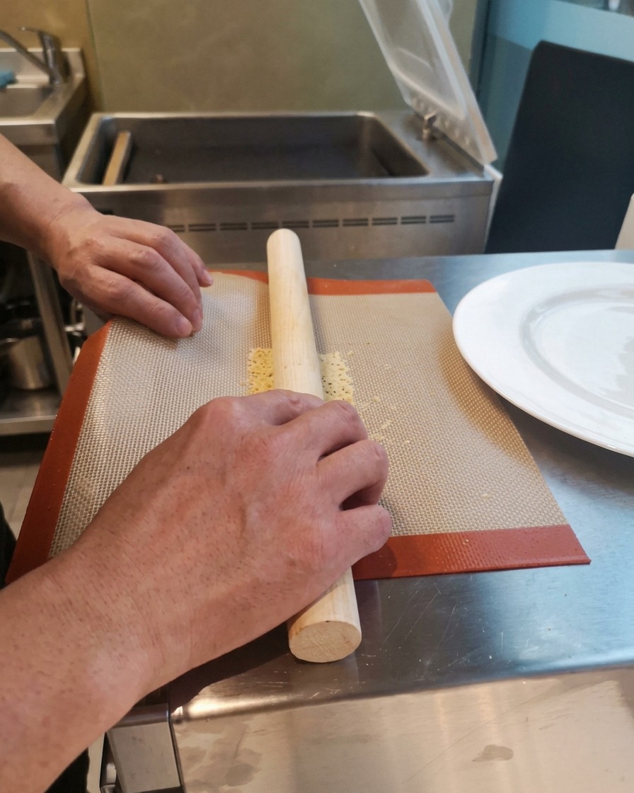 Hands carefully wrapping a hot, flexible baked crisp around a wooden rolling pin on a silicone baking mat.
