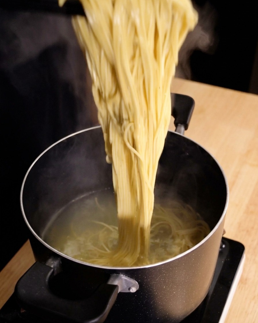 A large cluster of steaming cooked spaghetti noodles being lifted straight up out of a pot of hot water with tongs.