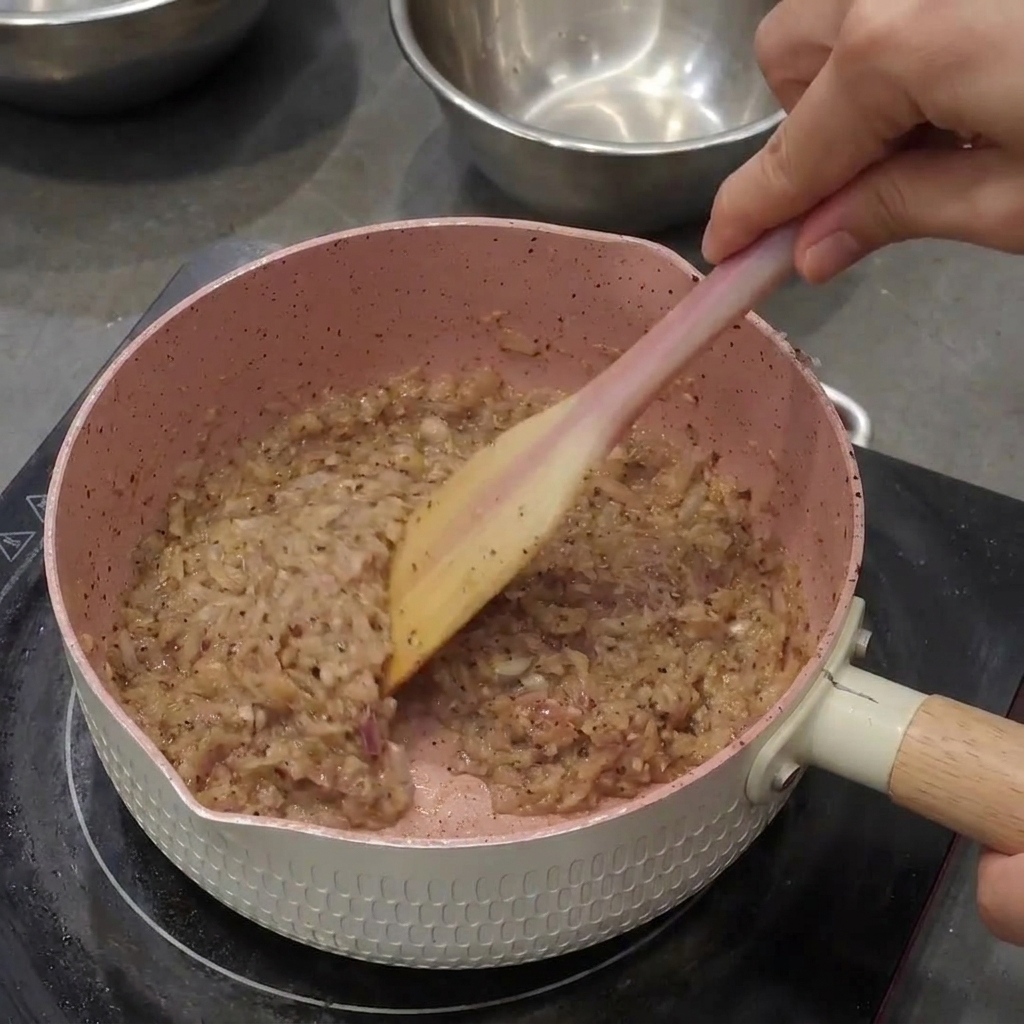 Stirring black pepper into sautéed onions and garlic, forming a dark and coarse paste.