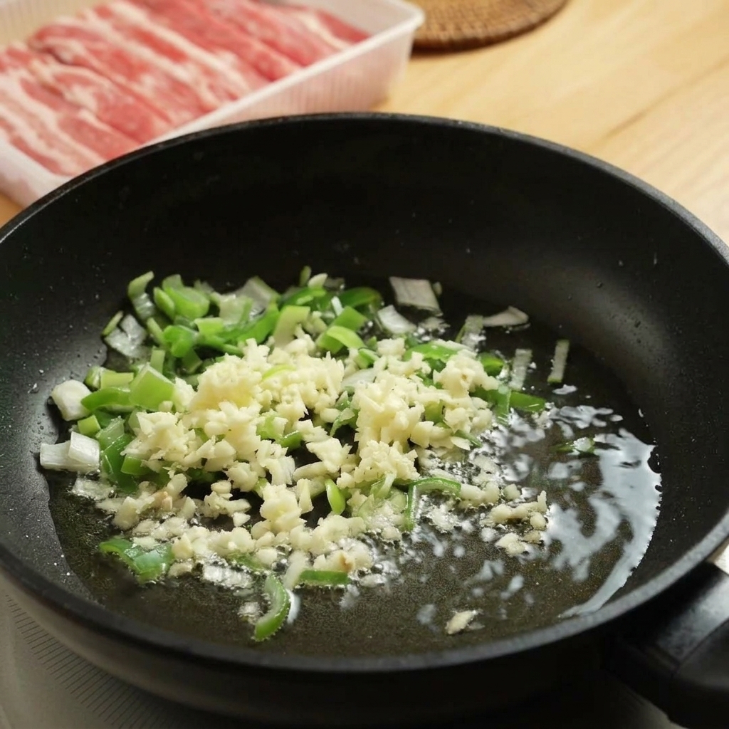 Chopped green scallions and minced white garlic sizzling in a small amount of hot oil inside a black frying pan.